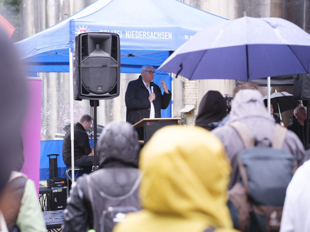 Der Bremer Bürgermeister Andreas Bovenschulte als Redner mit Mikrofon vor Teilnehmerinnen und Teilnehmern unter Regenschirmen am Bunker Valentin.