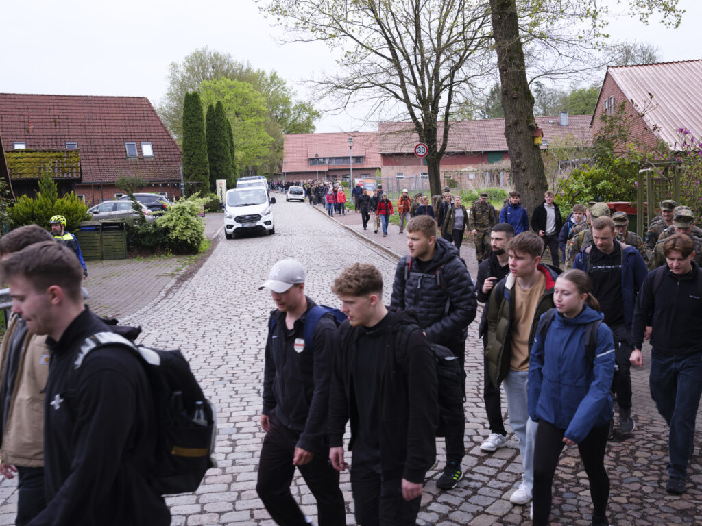 ange Gruppe junger Menschen läuft auf einem Weg durch eine von Bäumen gesäumte Landschaft.