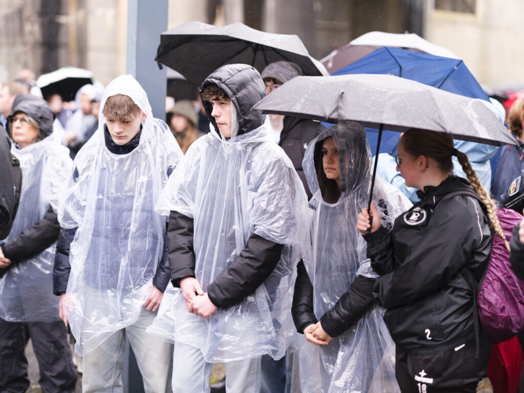 Jugendliche in transparenten Regenponchos und eine Polizistin unter einem Regenschirm beim Gedenkmarsch.