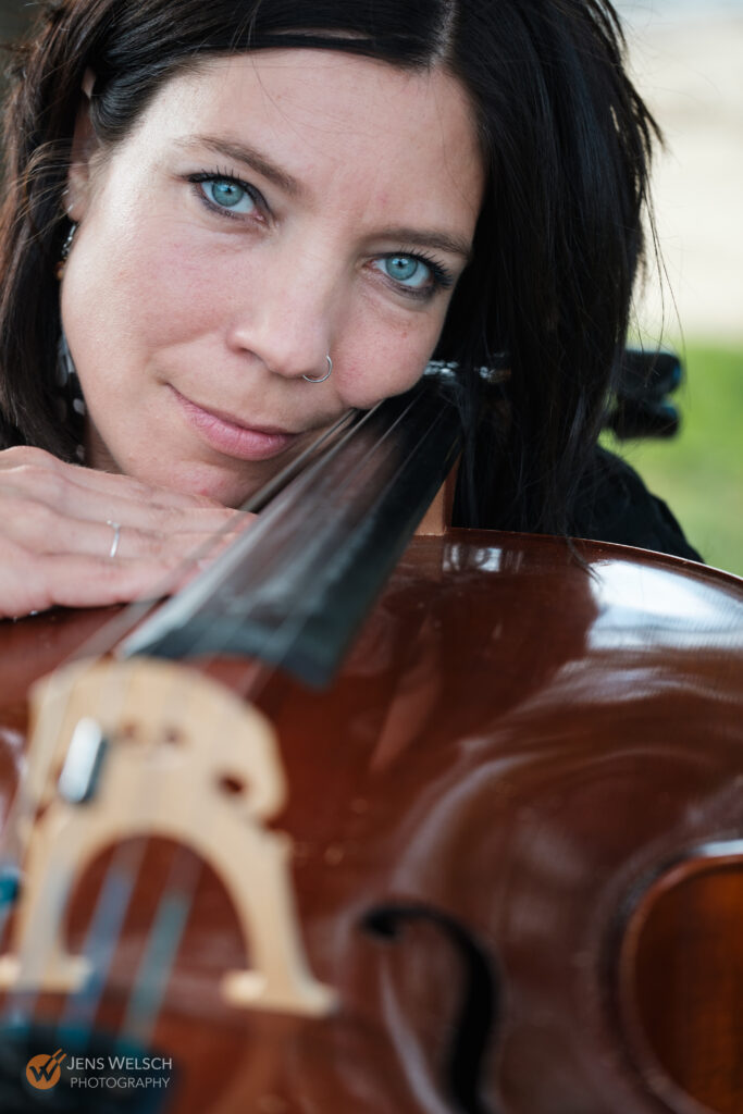 Nahaufnahme einer Cellistin mit intensivem Blick, die ihren Kopf an das Griffbrett ihres Cellos lehnt.