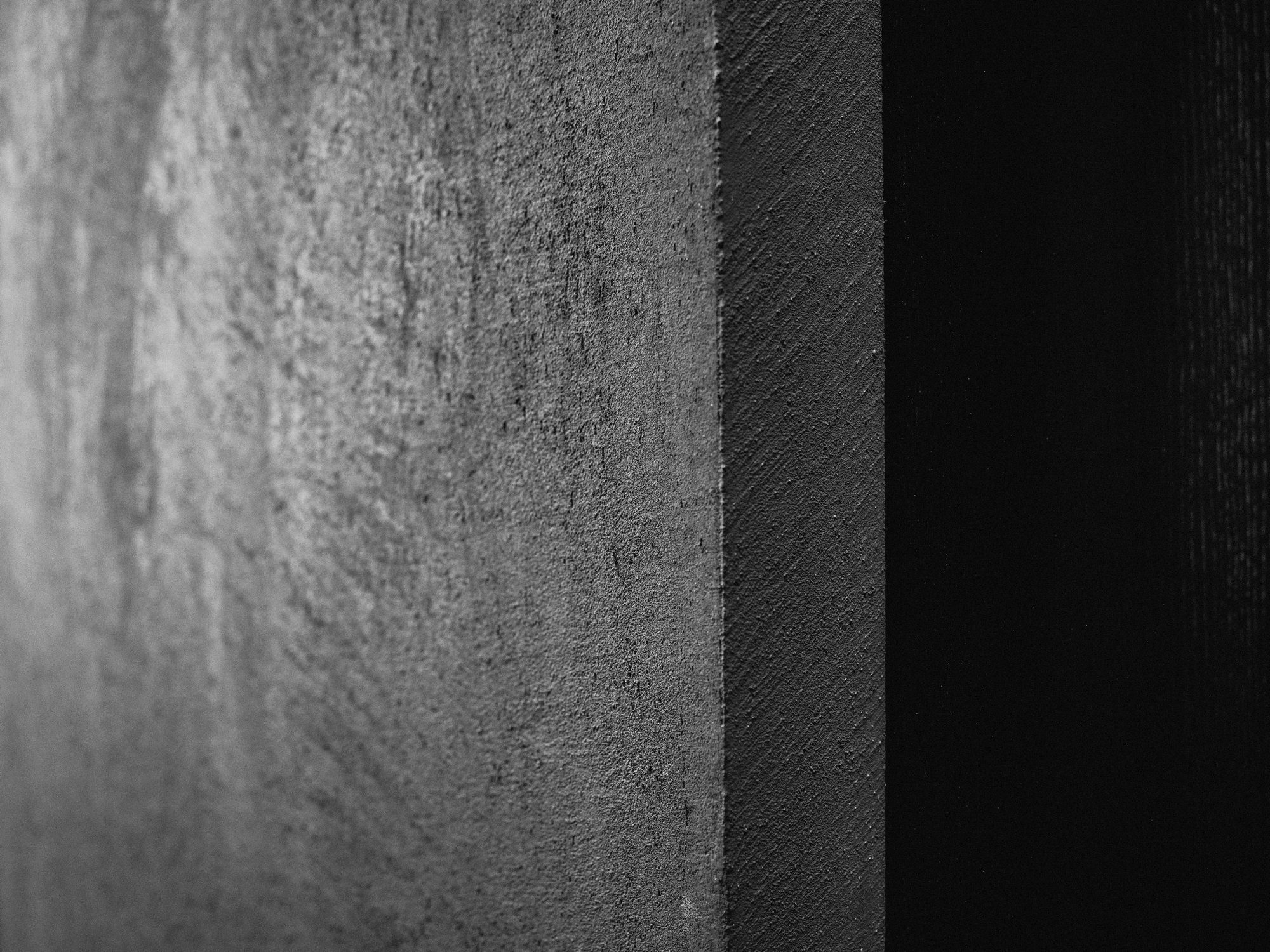 Schwarzweißes Detail einer gespachtelten Wand mit Kante und unterschiedlichen Oberflächenstrukturen.