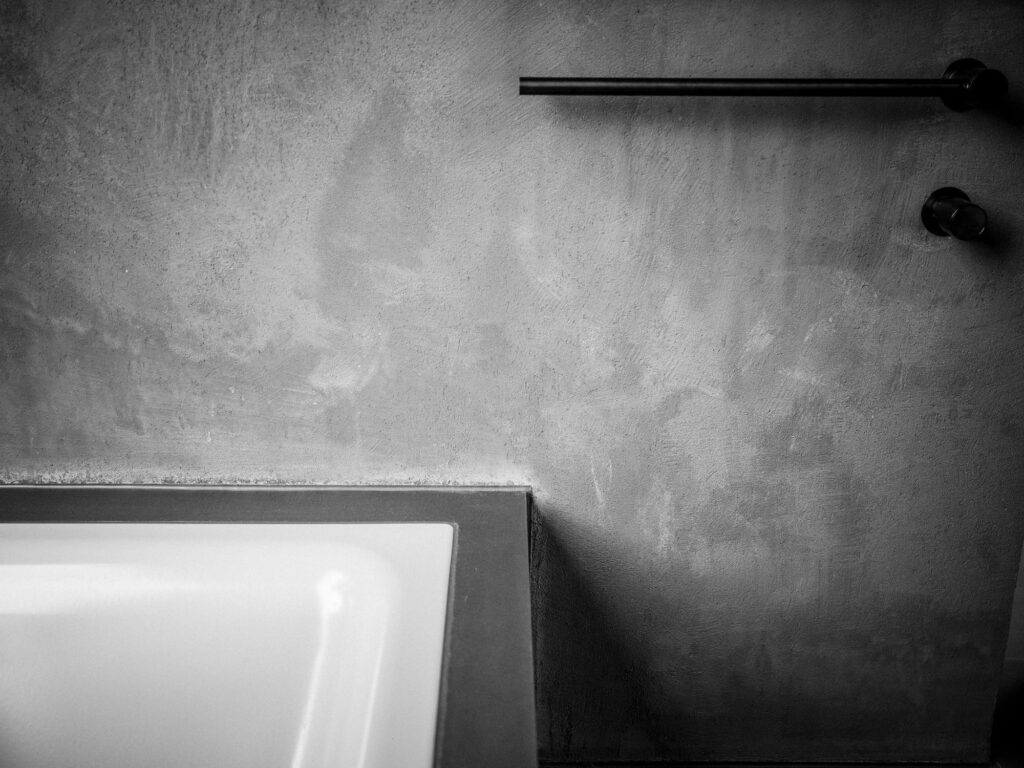Schwarzweißes Detail einer gespachtelten Badezimmerwand mit schwarzer Handtuchstange und Armatur.