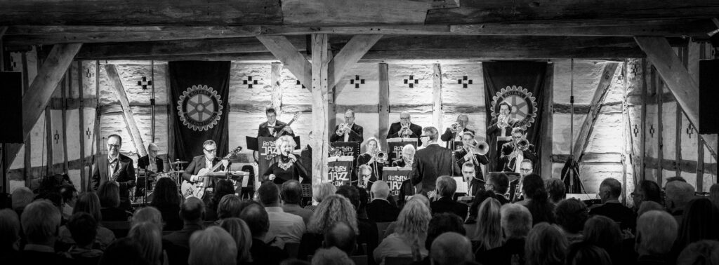 Panoramaaufnahme der gesamten Bigband auf einer Bühne mit Fachwerk-Hintergrund und Zuschauern im Vordergrund, Bötjersche Scheune in Worpswede