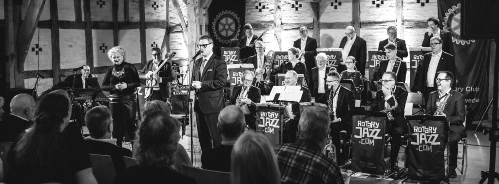 Die gesamte Bigband steht für den Abschlussapplaus auf der Bühne vor sitzendem Publikum.