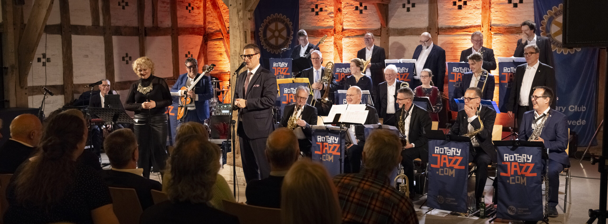 Die gesamte Bigband steht für den Abschlussapplaus auf der Bühne vor sitzendem Publikum.