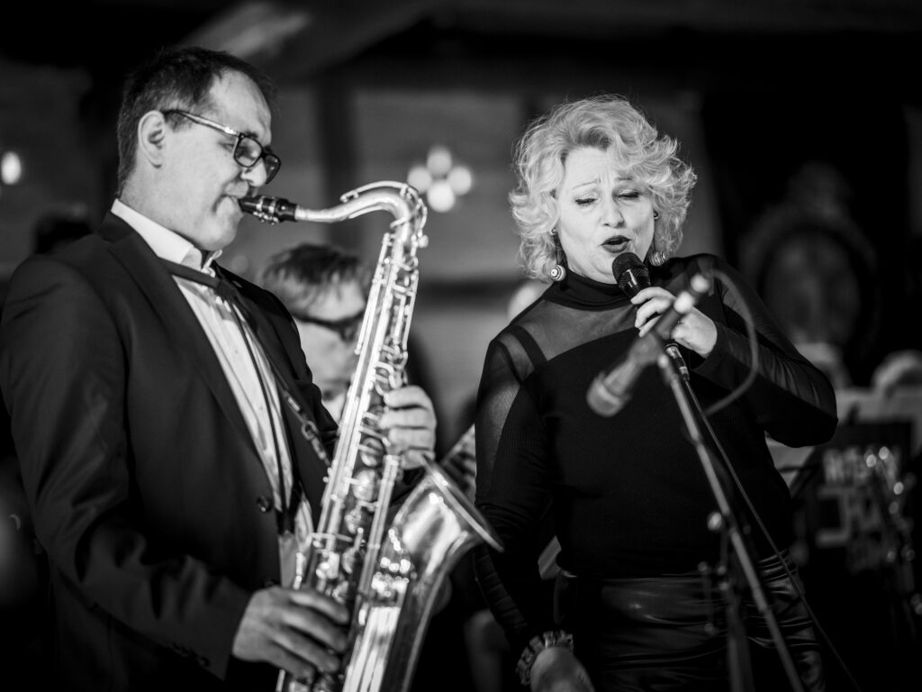 Duett aus einem Saxophonisten und einer Sängerin mit Mikrofon auf der Bühne in Schwarz-Weiß.