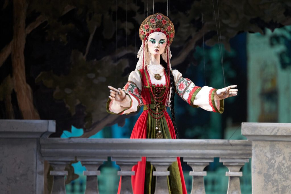 Weibliche Marionette mit aufwendig gearbeitetem Kopfschmuck und rot-grünem Kostüm auf der Bühne.